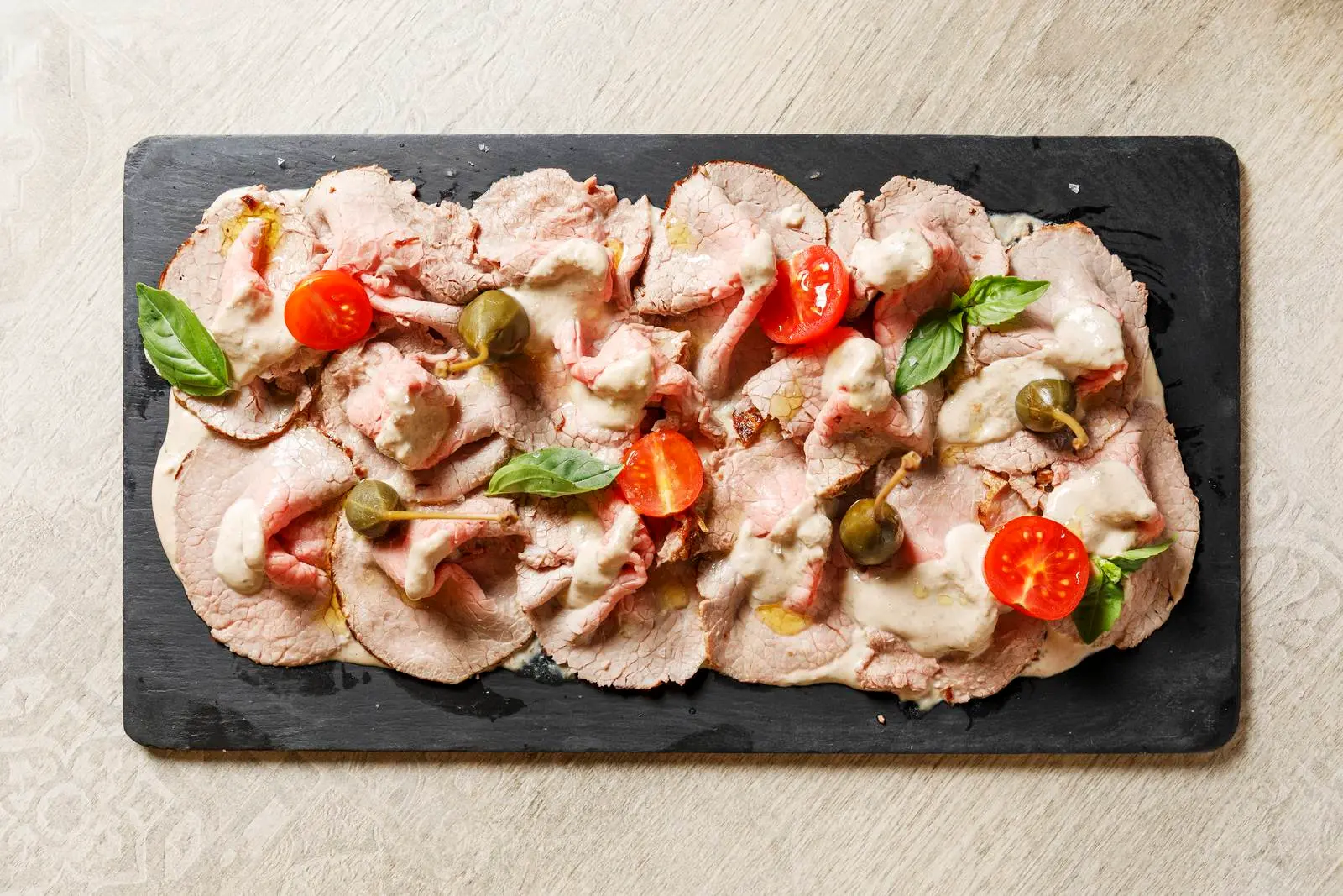 Sliced meat with capers, tomatoes and creamy sauce at ENCANTO