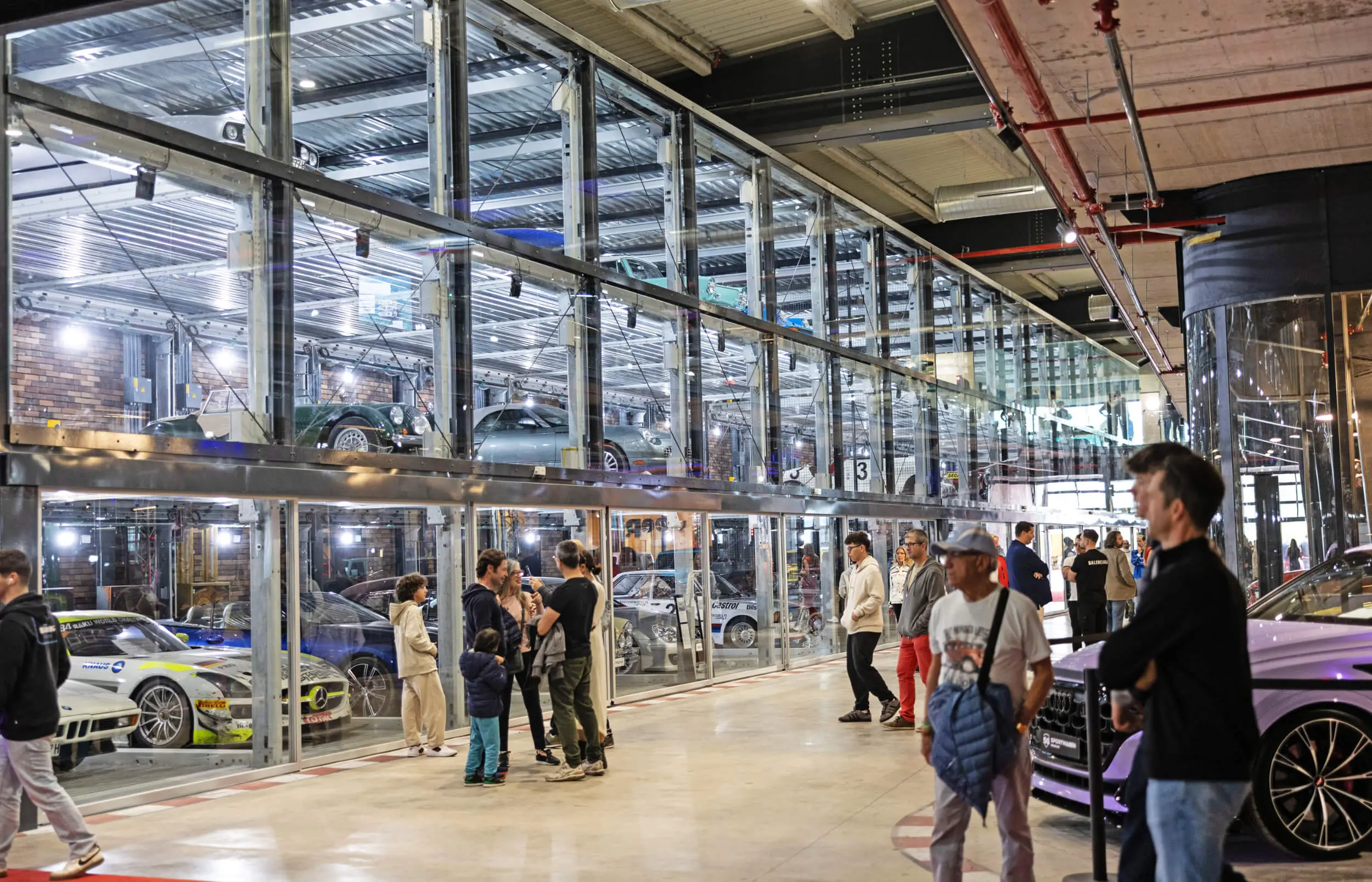 Visitors walking past glass car displays at Motorworld Mallorca